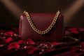 Burgundy leather crossbody bag with gold chain on dark velvet with roses